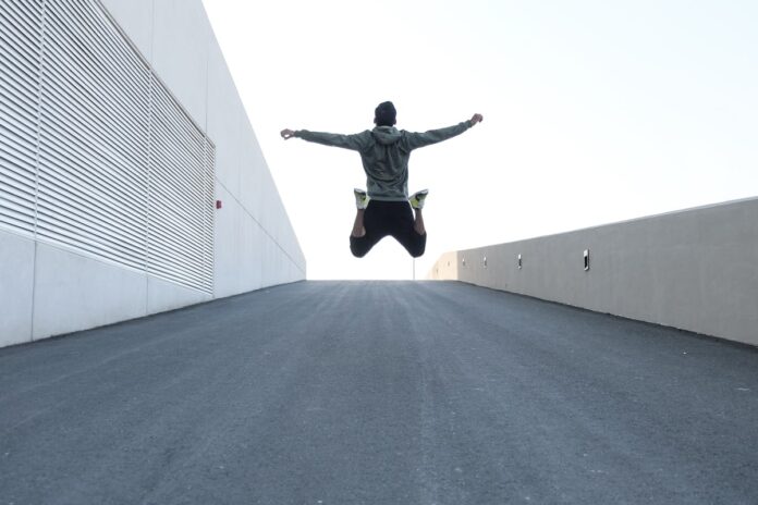 Man jumping on urban road with arms spread wide in Dubai, showcasing freedom and energy.