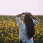 Woman in white shirt enjoying a sunny day in a blooming flower field.