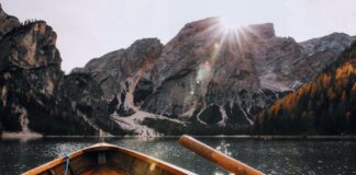 Wooden boat sailing on a serene mountain lake with sunrays illuminating the scenic landscape.