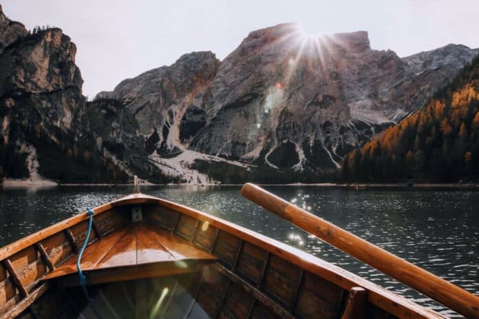 Wooden boat sailing on a serene mountain lake with sunrays illuminating the scenic landscape.